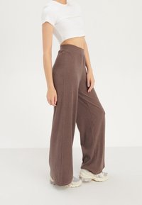 Bruna ribbade vida byxor med elastisk midjeband, matchade med en cropped vit T-shirt med kort ärm och ljusa träningsskor.