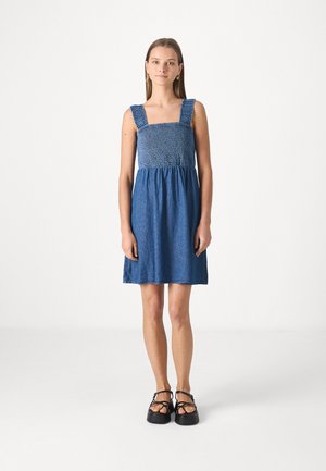 Robe en denim bleu avec un buste froncé, des bretelles larges et une jupe évasée. La robe est au-dessus des genoux et a une texture douce.
