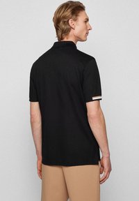 Svart polo skjorta, korta ärmar, mjukt bomullsmaterial. Har kontrasterande ränder vid ärmsluten, klassisk krage och en skräddarsydd passform.