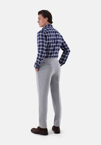 Camicia a quadri da uomo in blu navy e bianco, abbinata a pantaloni grigio chiaro su misura. Nota il dettaglio della tasca posteriore e le scarpe marroni scure.