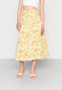 Saia midi floral em amarelo e branco com cintura ajustada e design fluido. Combinada com sandálias de slide amarelo claro.