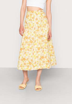 Saia midi floral em amarelo e branco com cintura ajustada e design fluido. Combinada com sandálias de slide amarelo claro.