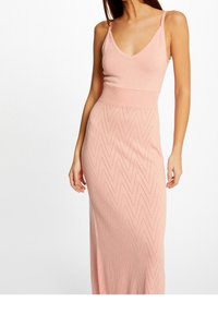 Longue robe rose avec un corsage ajusté à fines bretelles et une jupe texturée en zigzag avec une ceinture côtelée. Tissu tricoté léger.