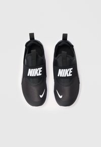 Chaussures noires à enfiler avec un dessus en tissu texturé, présentant une épaisse sangle noire avec "NIKE" en blanc et un Swoosh blanc à l'avant.