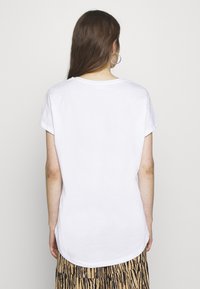 Tricou alb cu mânecă scurtă și decolteu rotund, având un tiv curbat și o textură moale, netedă. Purtați cu o fustă cu un model.