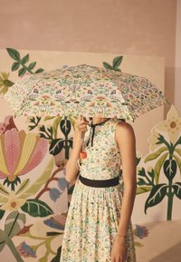 Lillemustriga vihmavari helekollase kangaga ja mänguliste graafikatega, millel on kaardus sang ja erksavärviline disain, hoitakse kleidi kohal.