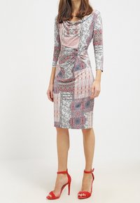 Musterkleid mit einem Schalkragen, Dreiviertelärmeln und geraffter Seite. Es präsentiert eine Mischung aus roten und grauen Blumenmustern.