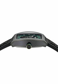 Kolfiberklocka med rektangulärt hölje, svart gummiband, gröna accenter på urtavlan och en framträdande rund krona. Texturerade detaljer synliga.