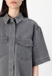 Grå denimskjorte med korte ermer, knappestolpekrage, to brystlommer og en myk, strukturert finish.