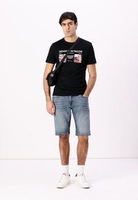 Svart kortermet t-skjorte med grafisk trykk, brukt med lyseblå denimshorts og hvite joggesko, komplementert med en liten svart crossover-taske.