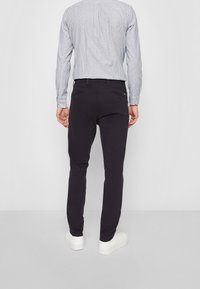 Czarne spodnie o wąskim kroju, wykonane z gładkiej tkaniny, z tylnymi kieszeniami i paskiem w talii. W połączeniu z jasną koszulą w kratę.