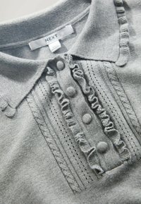 Grey knitted polo shirt featuring a frilled placket with decorative buttons and textured stripes along the neckline and body.