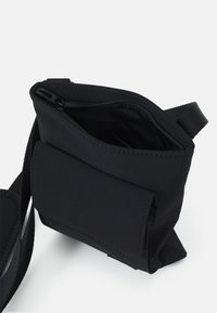 Borsa a tracolla nera in tessuto morbido con scomparto principale con cerniera e tasca frontale a pattina. Dotata di una tracolla regolabile.