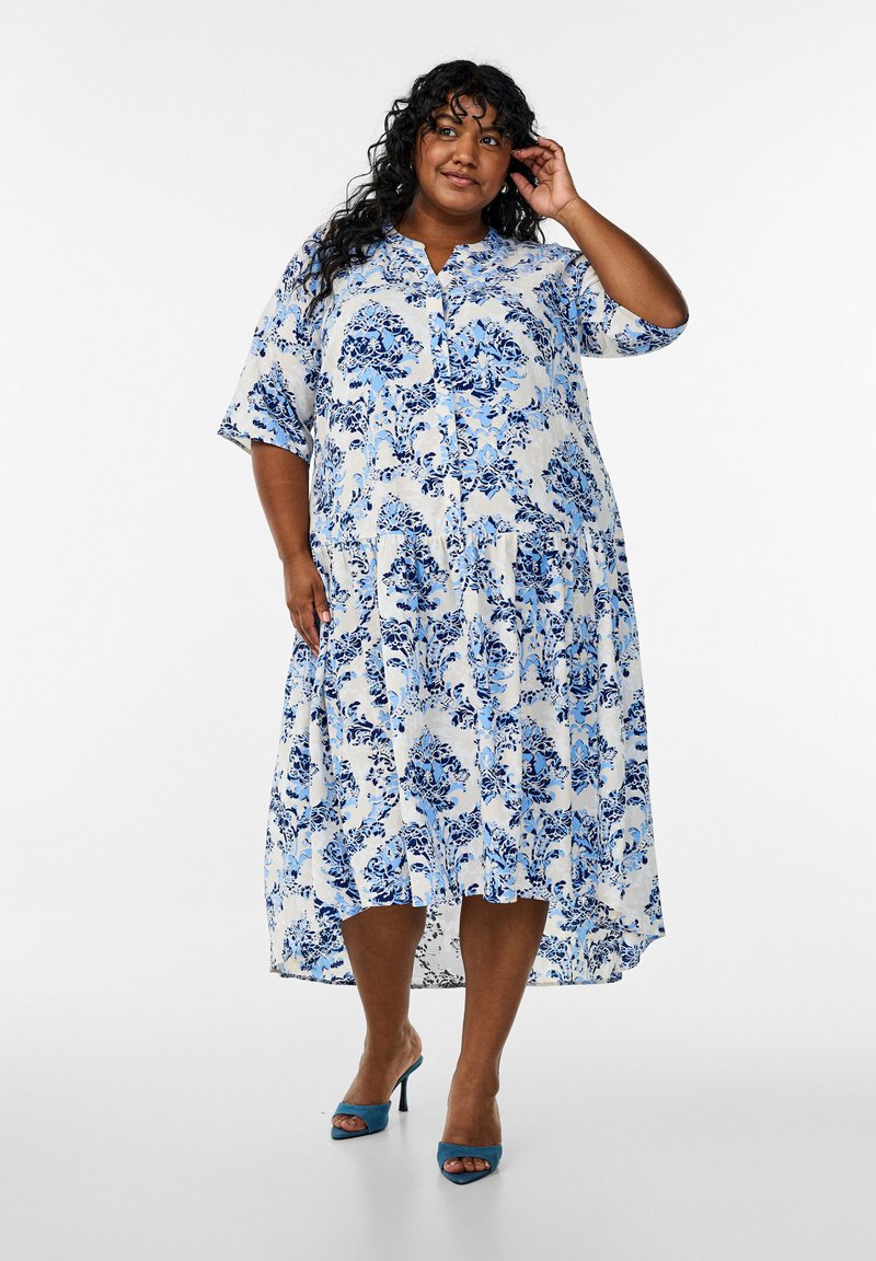 Robe chemise à imprimé floral bleu et blanc, avec des manches courtes, un devant boutonné et un design fluide avec un ourlet asymétrique.