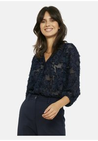 Marineblauwe doorschijnende blouse met textuurrijke bloemrijke versieringen, knoopsluiting aan de voorkant en driekwartmouwen. Glad materiaal en een ontspannen pasvorm.