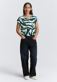 Haut à manches courtes, décolleté en V, imprimé zèbre avec des teintes turquoise et crème, associé à un pantalon droit en denim foncé et des baskets blanches.