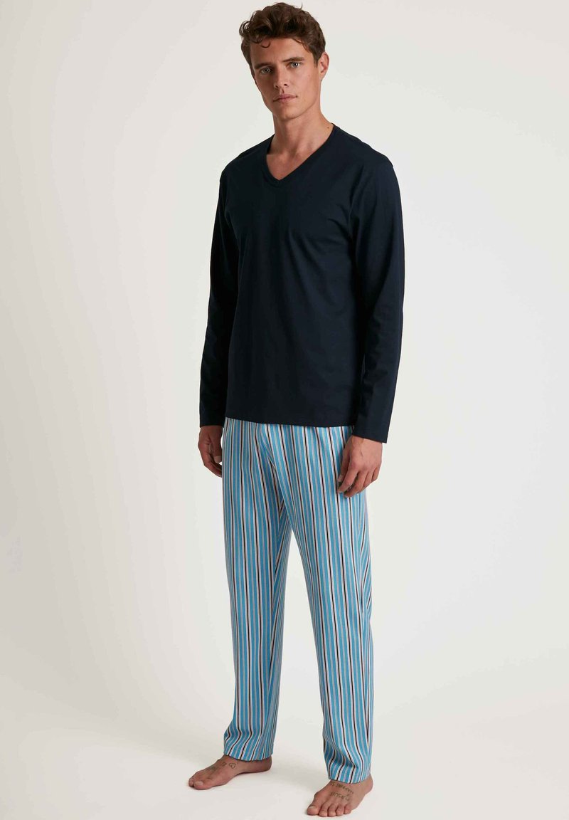 Langarmige marineblauwe V-hals top gecombineerd met blauwe gestreepte pyjamabroek met strepen van verschillende breedtes in blauw, wit en bruin.