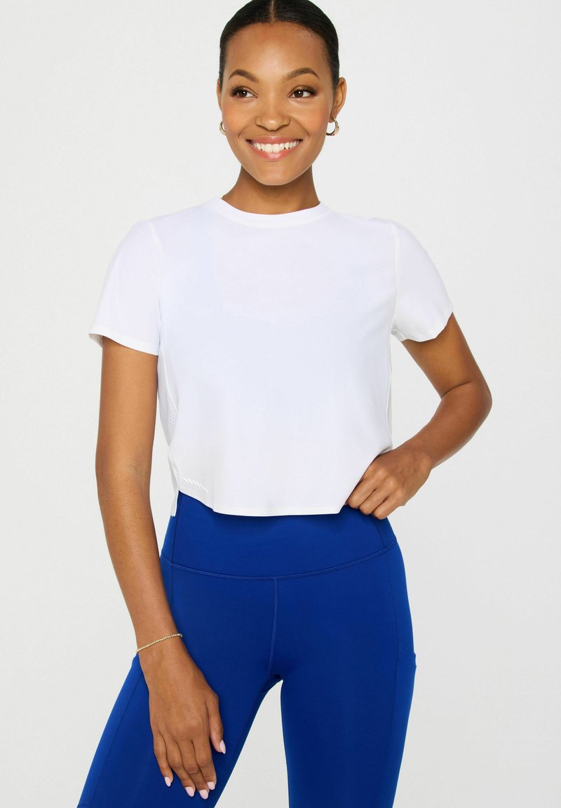 Weißes, kurzärmliges T-Shirt mit rundem Ausschnitt. Kombiniert mit hoch taillierten, schmalen blauen Leggings. Glatte Textur, minimales Design.