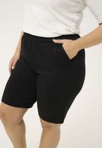 Shorts neri elasticizzati con vita elasticizzata, due tasche laterali e design aderente. Texture liscia, taglio alla ginocchia, senza motivi visibili.