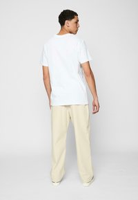 Hvid bomulds t-shirt med korte ærmer, rund hals og ensartet design, parret med lyse beige brede bukser og sneakers.