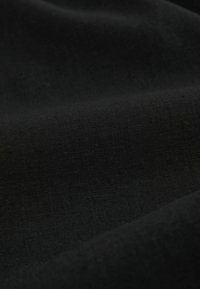 Gros plan sur un tissu noir lisse avec une texture subtile et de doux plis, mettant en valeur la qualité du matériau et le détail du tissage.