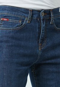 Donkerblauwe denim jeans met een rechte snit, voorzien van oranje stiksels, een klein rood label en een klassieke knoop- en ritsopening.