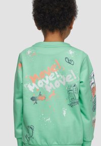 Zielony bawełniany sweatshirt z kolorowym napisem "Move!" oraz wesołymi ilustracjami, w tym kreskówkowymi jedzeniem i wzorem w stylu plamy z tyłu.