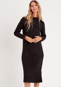 Vestido de punto negro con cuello simulado, mangas largas y silueta ajustada, que llega hasta la mitad de la pantorrilla. Textura suave.