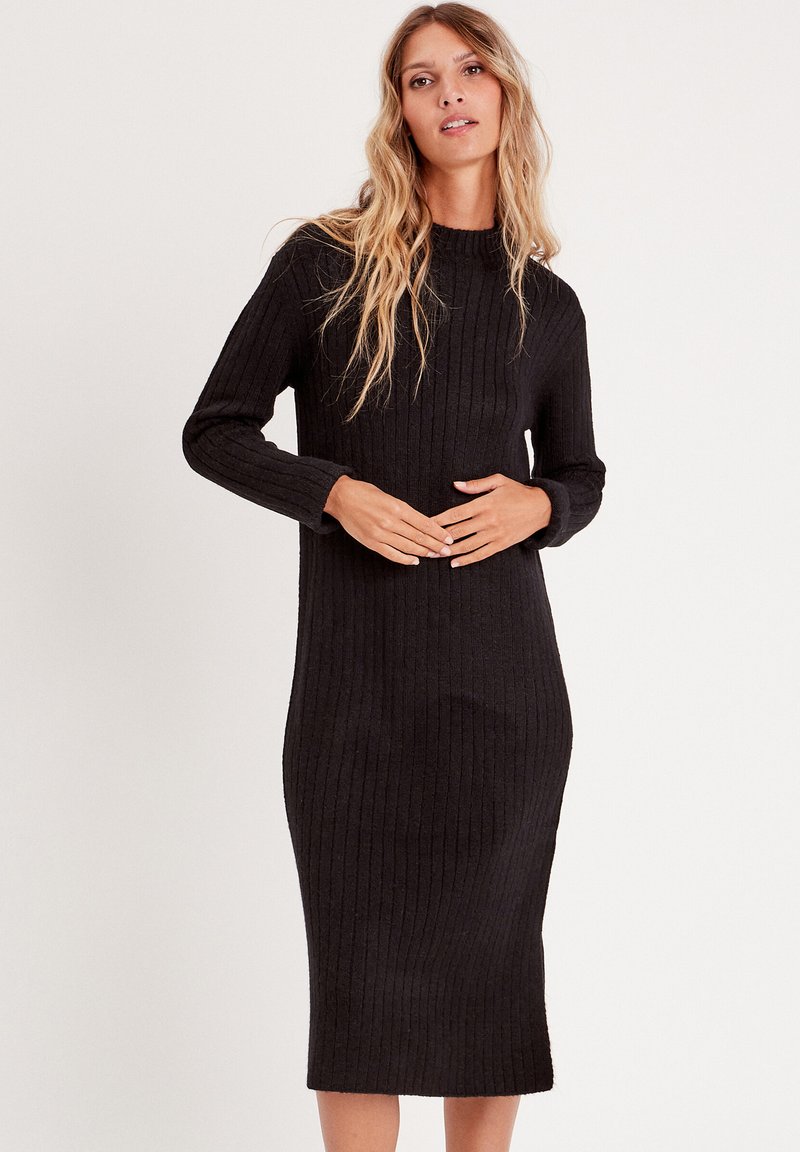 Vestido de punto negro con cuello simulado, mangas largas y silueta ajustada, que llega hasta la mitad de la pantorrilla. Textura suave.