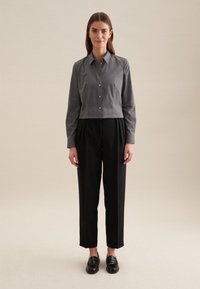 Camicia button-up grigia corta, pantaloni neri plissettati e mocassini neri. Design semplice con una texture liscia. Nessun motivo o decorazione.