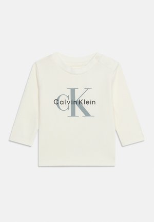 Weißes Babyoberteil mit langen Ärmeln und Calvin Klein "cK" Logo in Grau und Schwarz auf der Brust und Druckknöpfen an der Schulter.