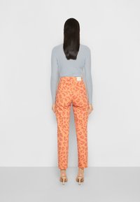 Suéter canoa azul claro e calças laranja com estampado de leopardo. As calças possuem cintura alta, perna reta e bolsos traseiros. Textura suave.