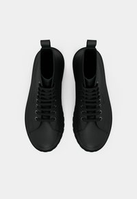 Pantofi negri tip high-top cu o finisare netedă, mată, având șase găuri pentru șireturi, șireturi și benzi de prindere pe călcâi. Talpă rotunjită.