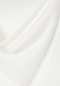Biely textil voľne prehodený, vystavujúci hladkú textúru a jemný lesk, s jemnými záhybmi a čistým, minimalistickým dizajnom.