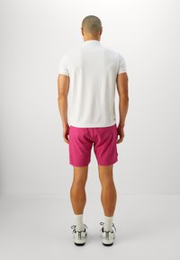 Men's outfit with a white polo shirt and pink shorts. The polo features short sleeves, while the shorts are above-the-knee length.