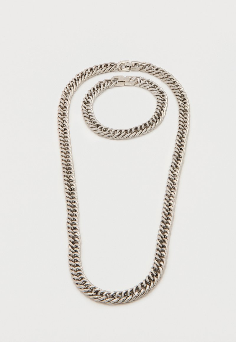 Ασημένιο χοντρό κολιέ με αλυσίδα και ταιριαστό βραχιόλι με διασταυρούμενους κρίκους και κουτιά κούμπωμα σε λευκό φόντο.