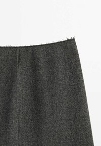 Tissu en laine gris foncé avec un bord supérieur brut et effiloché, montrant la texture et une couture verticale sur fond blanc.