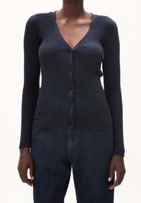 Námořnický žebrovaný cardigan s dlouhými rukávy, výstřihem do V a knoflíky vpředu. Vyrobený z pružného pleteného materiálu, těsně přiléhající k tělu.