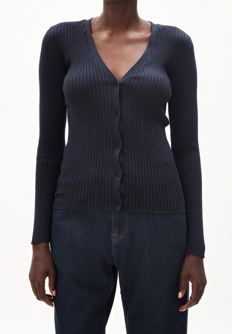 Námořnický žebrovaný cardigan s dlouhými rukávy, výstřihem do V a knoflíky vpředu. Vyrobený z pružného pleteného materiálu, těsně přiléhající k tělu.