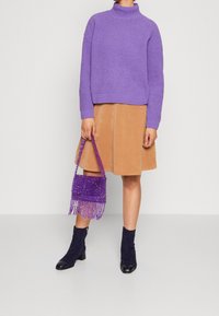 Violetti neulottu pooloneulepaita, ruskea mannapikkahame, violetti helmikoristeltu olkalaukku hapsuilla sekä mustat kimaltavat nilkkurit mustilla kärjillä.