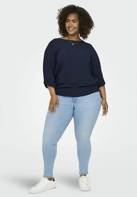 Maglietta blu navy a vestibilità ampia con maniche tre quarti, abbinata a jeans skinny blu chiaro e sneaker bianche, con risvolti alle maniche.