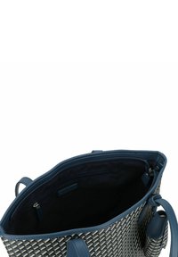Sac en toile tissé avec des poignées en cuir bleu, extérieur à motifs en blanc et marine, intérieur spacieux avec une poche zippée et doublure noire.