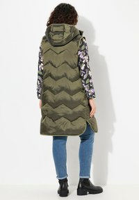 Grön, chevron-quiltad pufferväst med huva. Matchad med en blommig långärmad topp, blåjeans och svarta ankelskor.