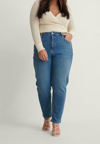 Světle krémový pletený crop top doplněný vysokým modrým denimovým džíny. Zbytek outfitu dotvářejí béžové sandály na řemínky.
