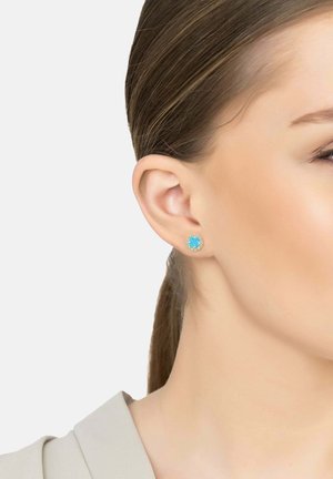 Turquoise stud earring with a circular design, surrounded by a clear stone halo. Silver-tone metal base. Positioned in an earlobe.