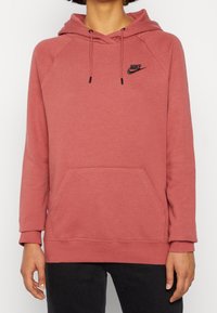 Rosa hoodie med framficka, justerbar dragsko i huvan och svart Nike-logotyp. Mjuk tyg med ribbad mudd och fåll.