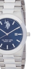 Orologio in acciaio inox argento con quadrante blu scuro, indici delle ore argento e display della data. Presenta un logo di un giocatore di polo.