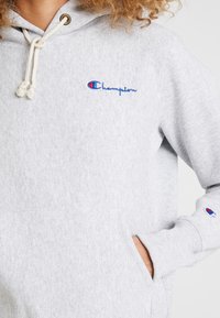 Grauer Fleece-Hoodie mit Kapuze und Kordelzug, Kängurutasche und aufgesticktem blauen "Champion"-Logo. Mit gerippten Bündchen und Saum.