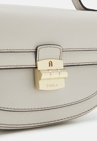 Ljusgrå läderhandväska med guldfärgad hårdvara, låsdetalj och kontrasterande sömmar längs kanterna. Slät textur och strukturerad design.