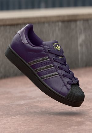 Purple leather sneaker featuring a black rubber toe cap, black stripes, and matching laces. Textured surface with a stitched design.